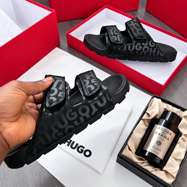 A pair of black HUGO sandals with a bold design and premium materials, presented in a luxurious setting with red boxes and high-end fragrance.