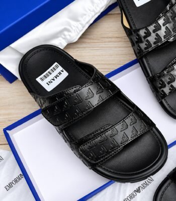 A pair of black leather slides with debossed logo design, presented in a blue box with white packaging, showcasing Modern Luxury and Urban Edge style.