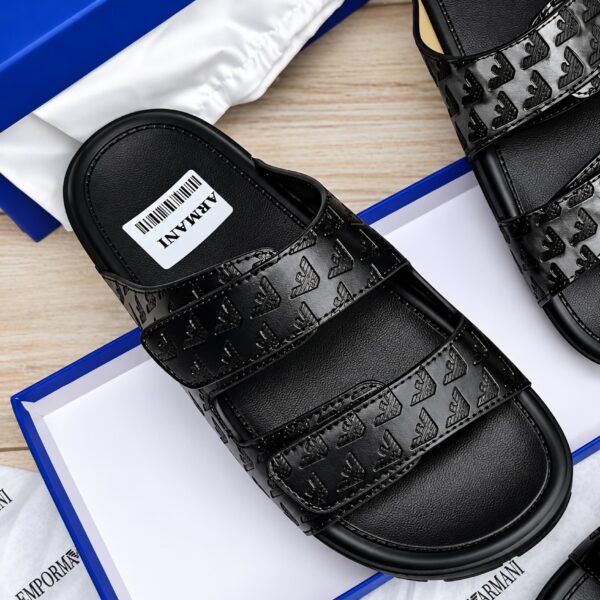 A pair of black leather slides with debossed logo design, presented in a blue box with white packaging, showcasing Modern Luxury and Urban Edge style.