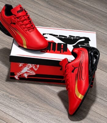 A pair of vibrant red Puma sneakers with gold and black accents, exuding Modern Luxury and Urban Edge, placed elegantly on a wooden floor next to their box.
