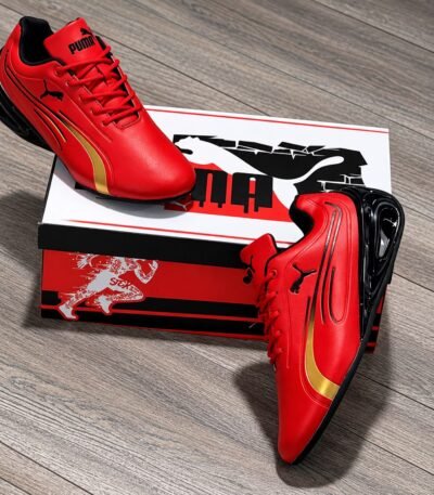A pair of vibrant red Puma sneakers with gold and black accents, exuding Modern Luxury and Urban Edge, placed elegantly on a wooden floor next to their box.