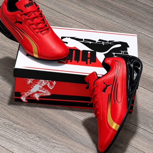 A pair of vibrant red Puma sneakers with gold and black accents, exuding Modern Luxury and Urban Edge, placed elegantly on a wooden floor next to their box.